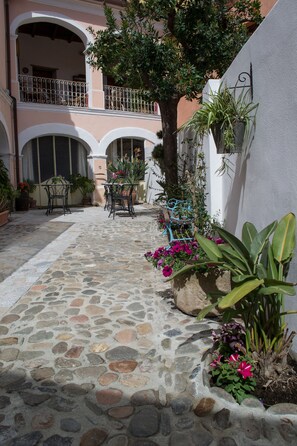 A courtyard with stone flooring, outdoor seating, potted plants, and a building with balconies. - B&B Casa Licheri (San Vito)