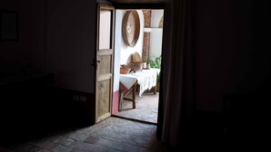 Un interior rústico con una puerta de madera que da a un comedor, con pared de ladrillo, una cesta tejida y una mesa dispuesta con cuencos y una planta.