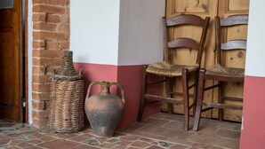 Rincón con una cesta de mimbre, una jarra de cerámica y dos sillas de madera frente a una pared con decoración roja y blanca.