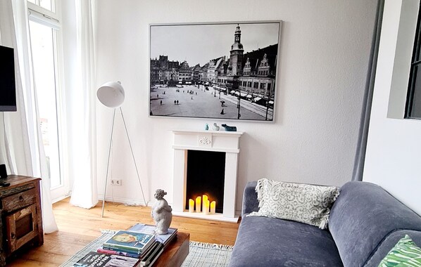 Ein Wohnzimmer mit Kamin, einer Couch, einem Couchtisch mit Büchern und einem gerahmten Bild an der Wand.