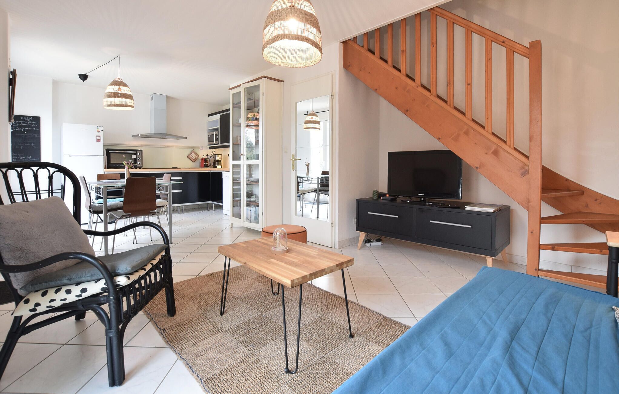 Una sala de estar moderna con un sofá, un comedor con sillas, una cocina al fondo y una escalera de madera.