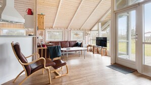 Un'ampia stanza con soffitto alto, pareti in legno, un'ampia finestra, un divano, un tavolo da pranzo e una televisione.