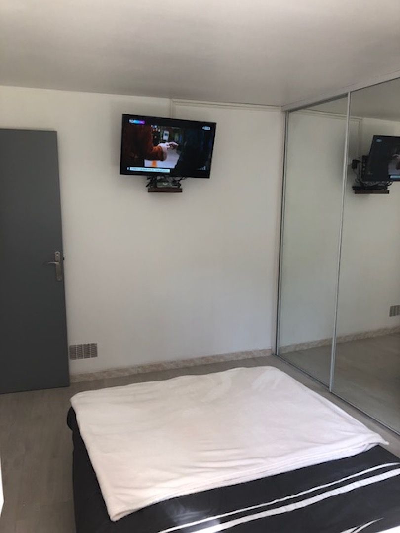 Hotellihuone, jossa on sänky, seinälle asennettu televisio ja liukuovilla varustettu vaatekaappi.