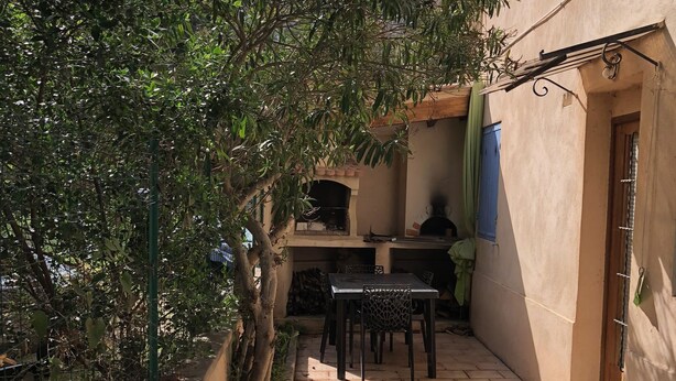Un patio con mesa y sillas, suelo de ladrillo y un edificio con puerta y ventanas.