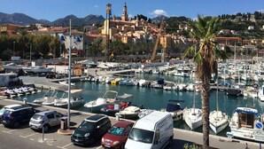Un puerto deportivo con barcos amarrados, una camioneta blanca y montañas al fondo.