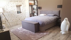 Um quarto com uma cama, uma estante, um abajur, uma escultura branca e uma parede de pedra.