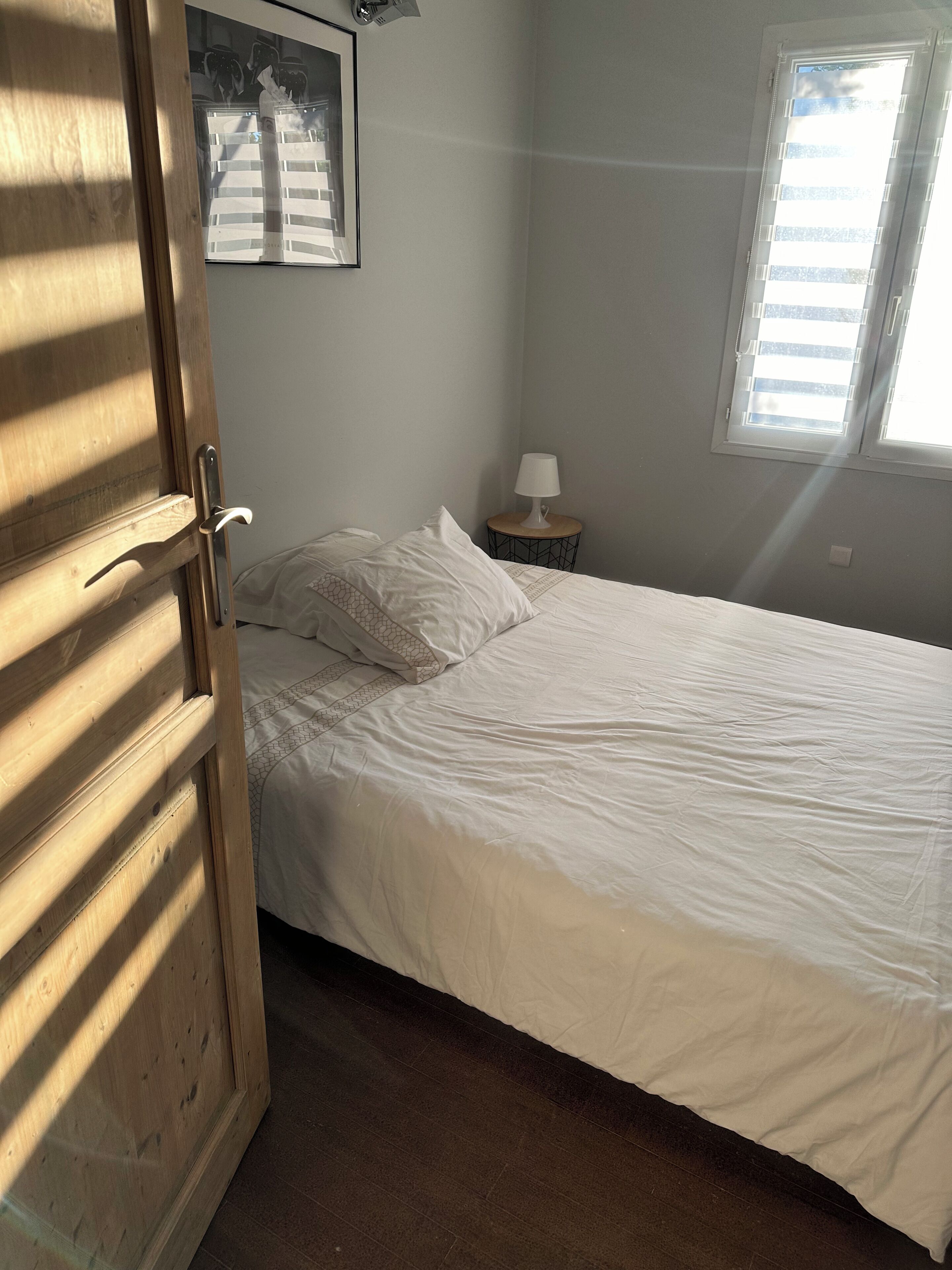 Un dormitorio con cama, mesita de noche, lámpara, ventana y puerta.