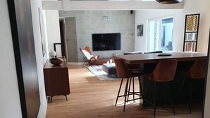 Uma sala de estar ampla com piso de madeira, uma mesa de jantar com cadeiras, uma televisão e uma lareira.