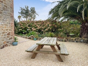 Enjoy a serene garden with a rustic picnic table surrounded by lush flowering shrubs and a tall palm tree.