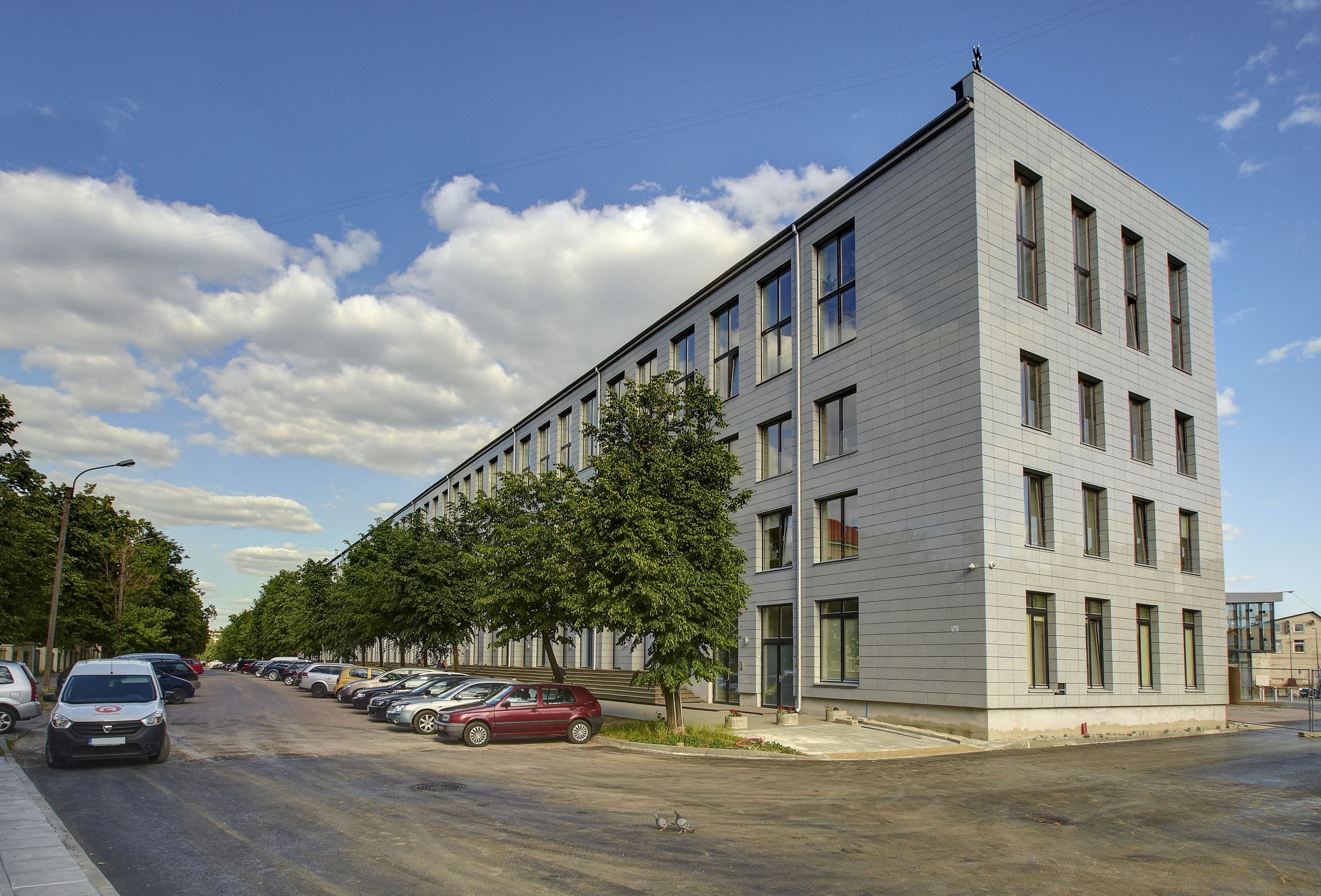 Ein modernes Gebäude mit einer Reihe geparkter Autos an einer von Bäumen gesäumten Straße.