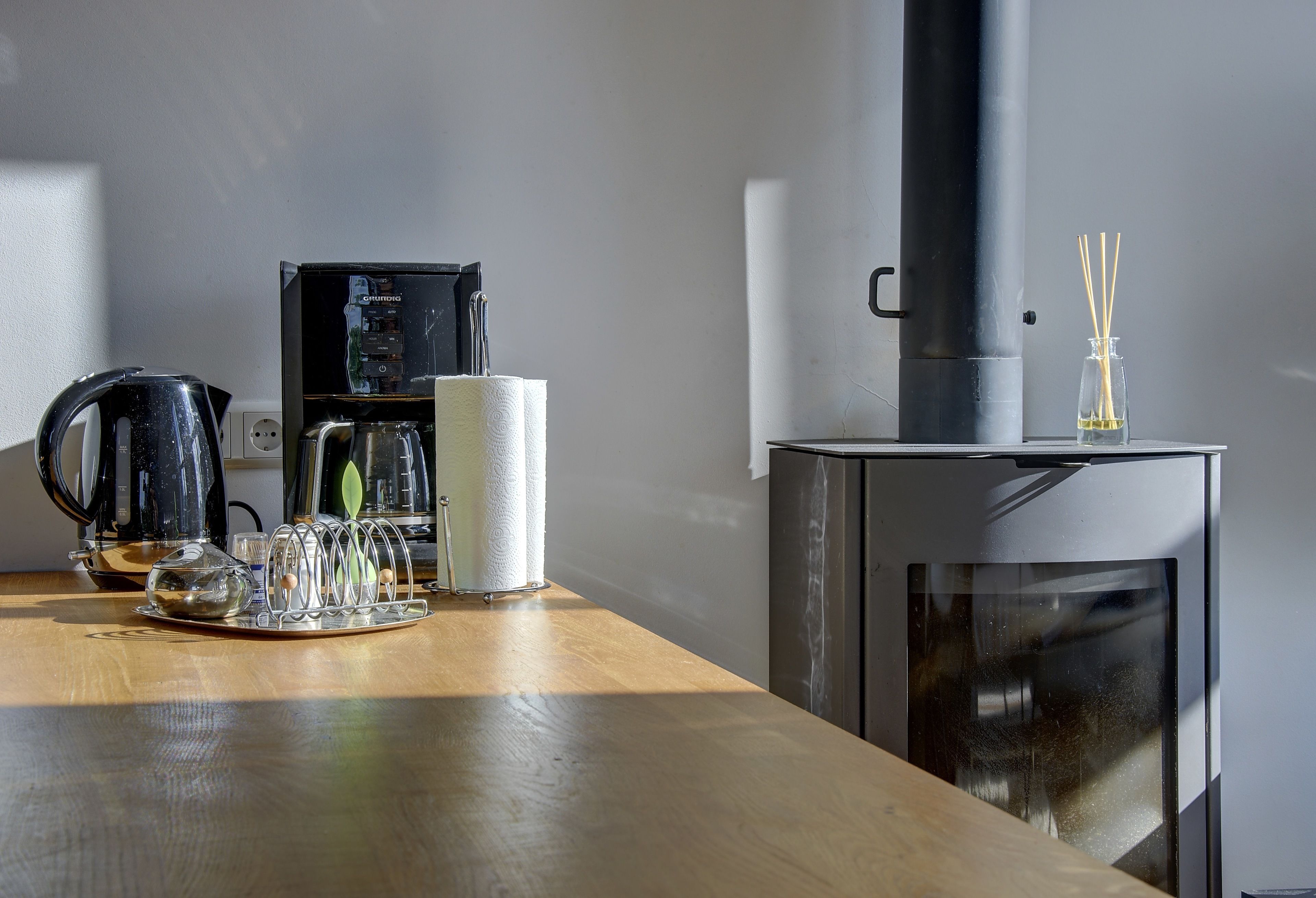 Een keuken met een koffiezetapparaat, waterkoker en een glazen pot op het aanrecht.
