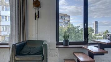 A modern living room with a leather sofa, a wooden bench, a potted plant, and a view of buildings through a large window.