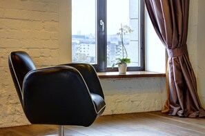 A room with a black leather chair, a window with a view of buildings, and a potted plant on the windowsill.