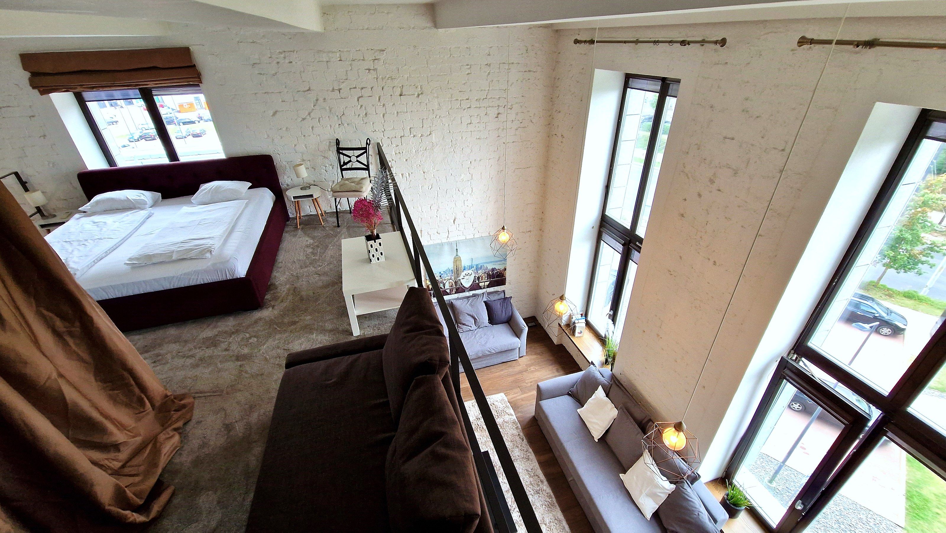 A bedroom with a large bed, a sitting area with a sofa, and a view of the outside through large windows.