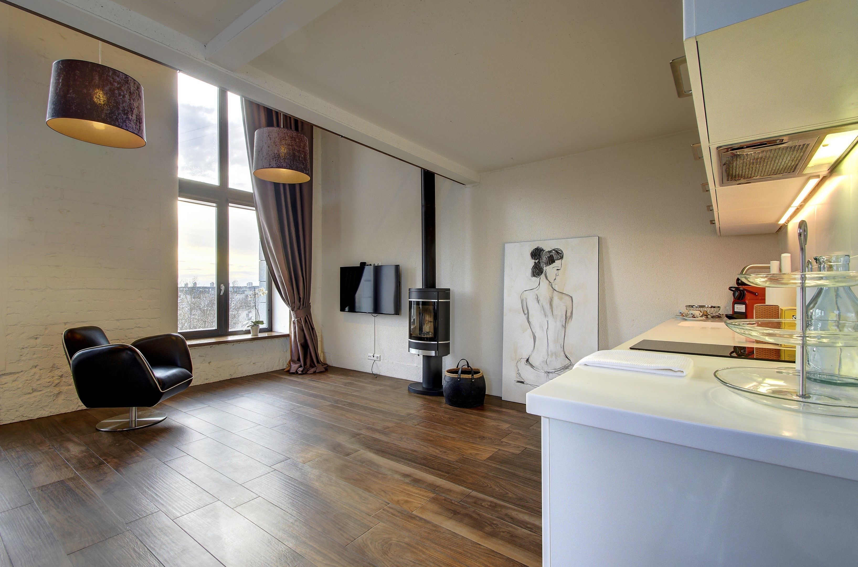 A modern room with a large window, a black leather chair, a wood-burning stove, and a glass coffee table.
