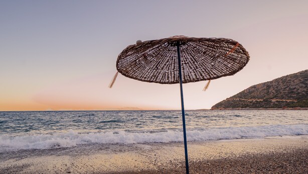 A beach umbrella on a pebbly shore with the ocean and a distant mountain in the background. - Karia Apart (Datça)