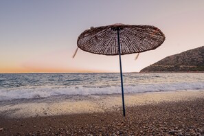 A beach umbrella on a pebbly shore with the ocean and a distant mountain in the background. - Karia Apart (Datça)