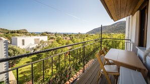 A balcony with a wooden table and chairs, overlooking a lush garden and distant hills. - Karia Apart (Datça)