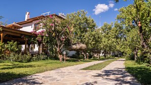 A stone pathway leading through a lush garden with a white building on the left. - Karia Apart (Datça)