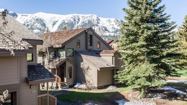 A two-story house with a covered porch and a view of snow-capped mountains.