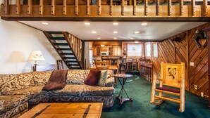 A cozy cabin interior with a wooden staircase, a sofa, a dining table, and a wooden rocking chair.