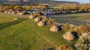 Un camping rural con varias tiendas de forma abovedada y algunos edificios al fondo.