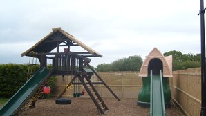 Un parque infantil con una estructura de madera para escalar, un tobogán verde y un columpio hecho con neumático.
