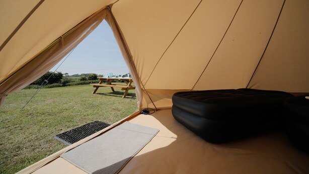 Una carpa con una mesa de picnic en el exterior, un área para dormir oscura en el interior y un campo cubierto de hierba al fondo.