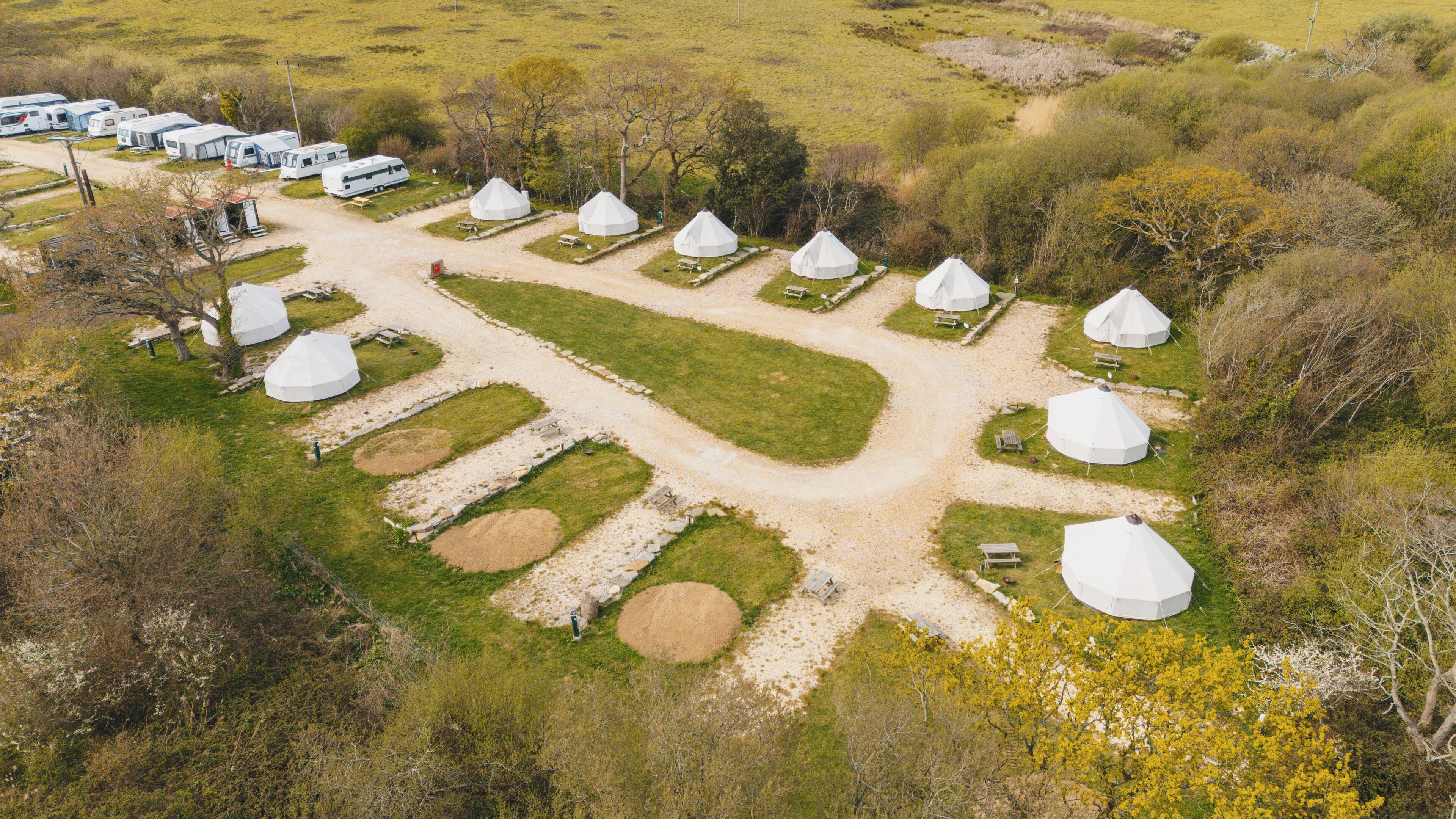 A campsite with yurts arranged in a circular pattern, surrounded by grassy areas and trees.