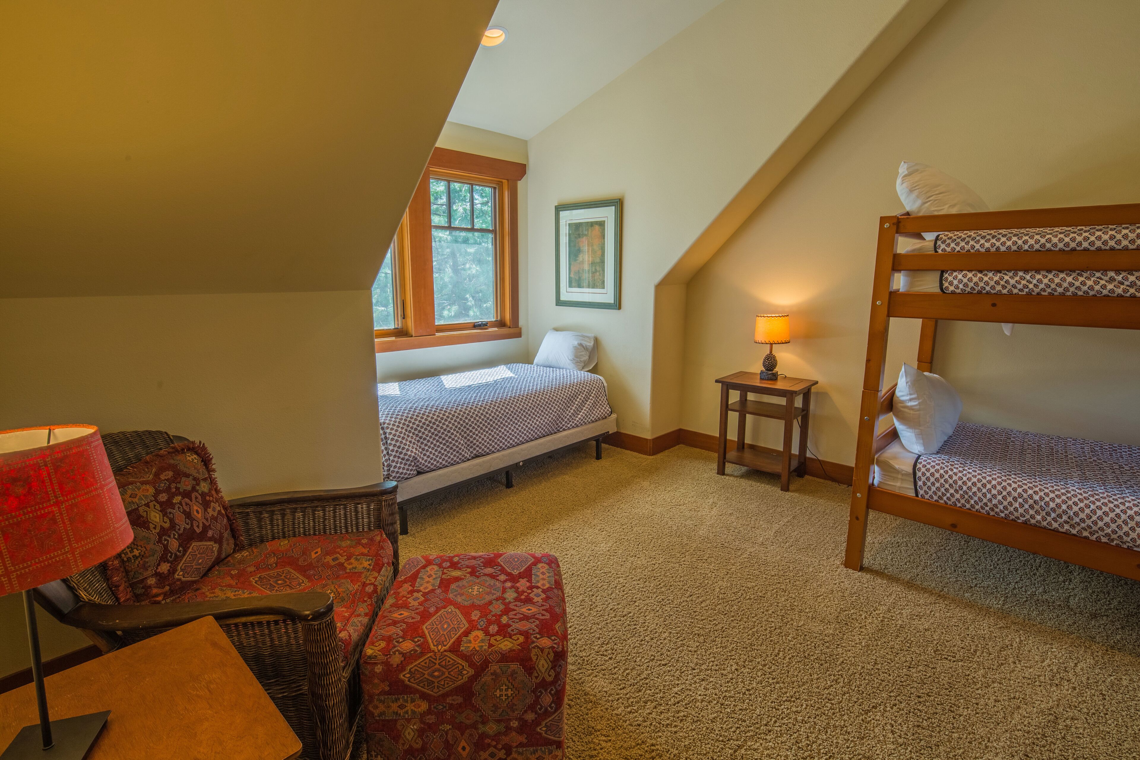 A cozy attic bedroom with two beds, a small table, a lamp, and a window.