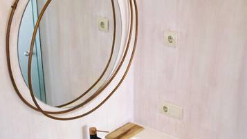 A bathroom with a white sink, wooden vanity, and a round mirror with a brass frame.