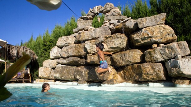 A rock formation in a swimming pool with a person climbing it. - Boutique Hostal Salinas (Sant Josep de sa Talaia)
