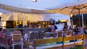 An outdoor seating area with wooden benches and tables, string lights, and a bar area with a counter and stools. - Boutique Hostal Salinas (Sant Josep de sa Talaia)