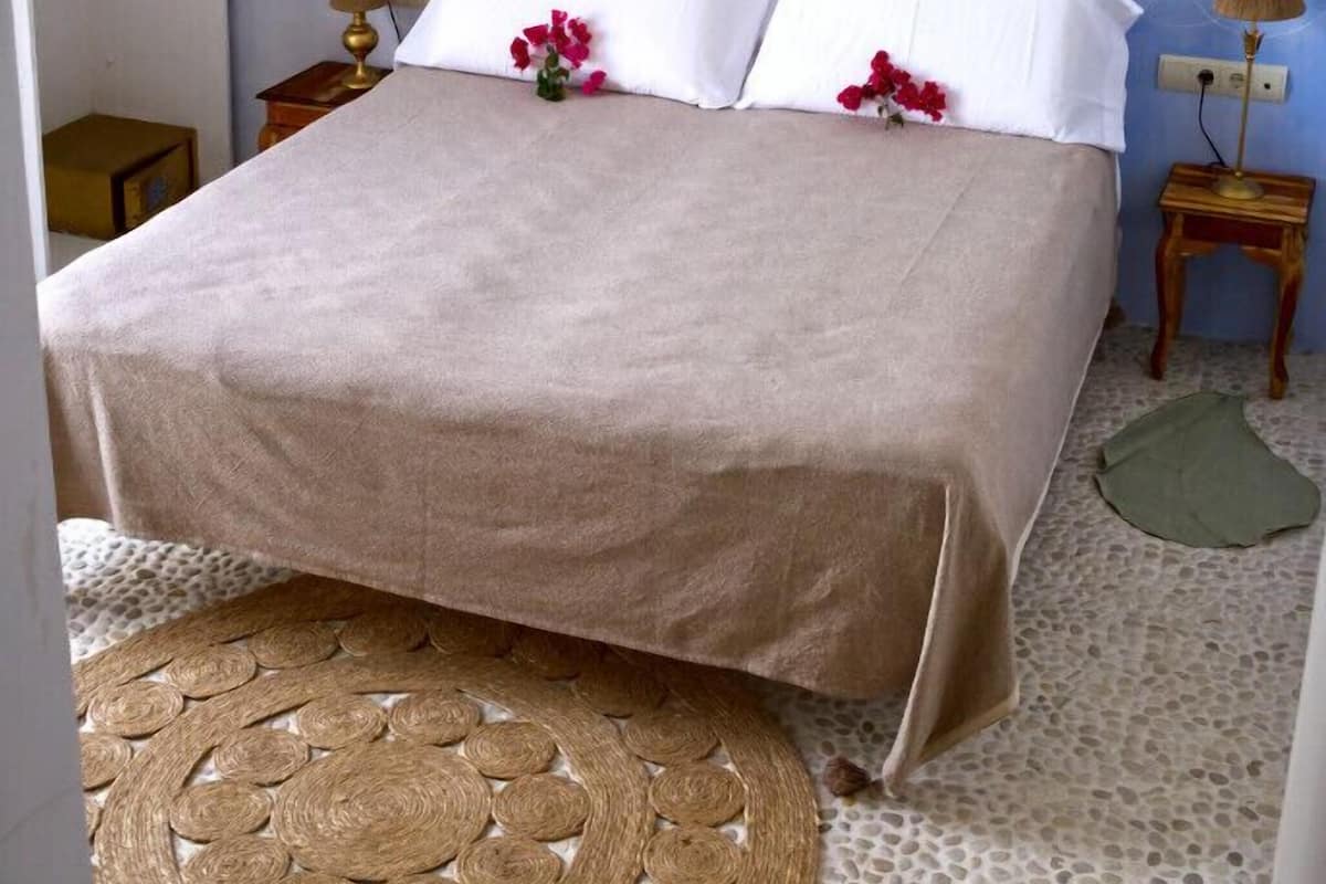 A neatly made bed with a beige bedspread, two white pillows, and a decorative wall hanging above.