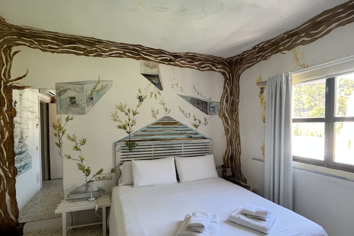 A bedroom with a bed, pillows, a nightstand, a lamp, and a window.