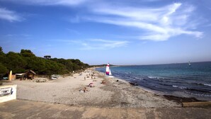 A beach with a sailboat, a small hut, and a lifeguard tower. - Boutique Hostal Salinas (Sant Josep de sa Talaia)