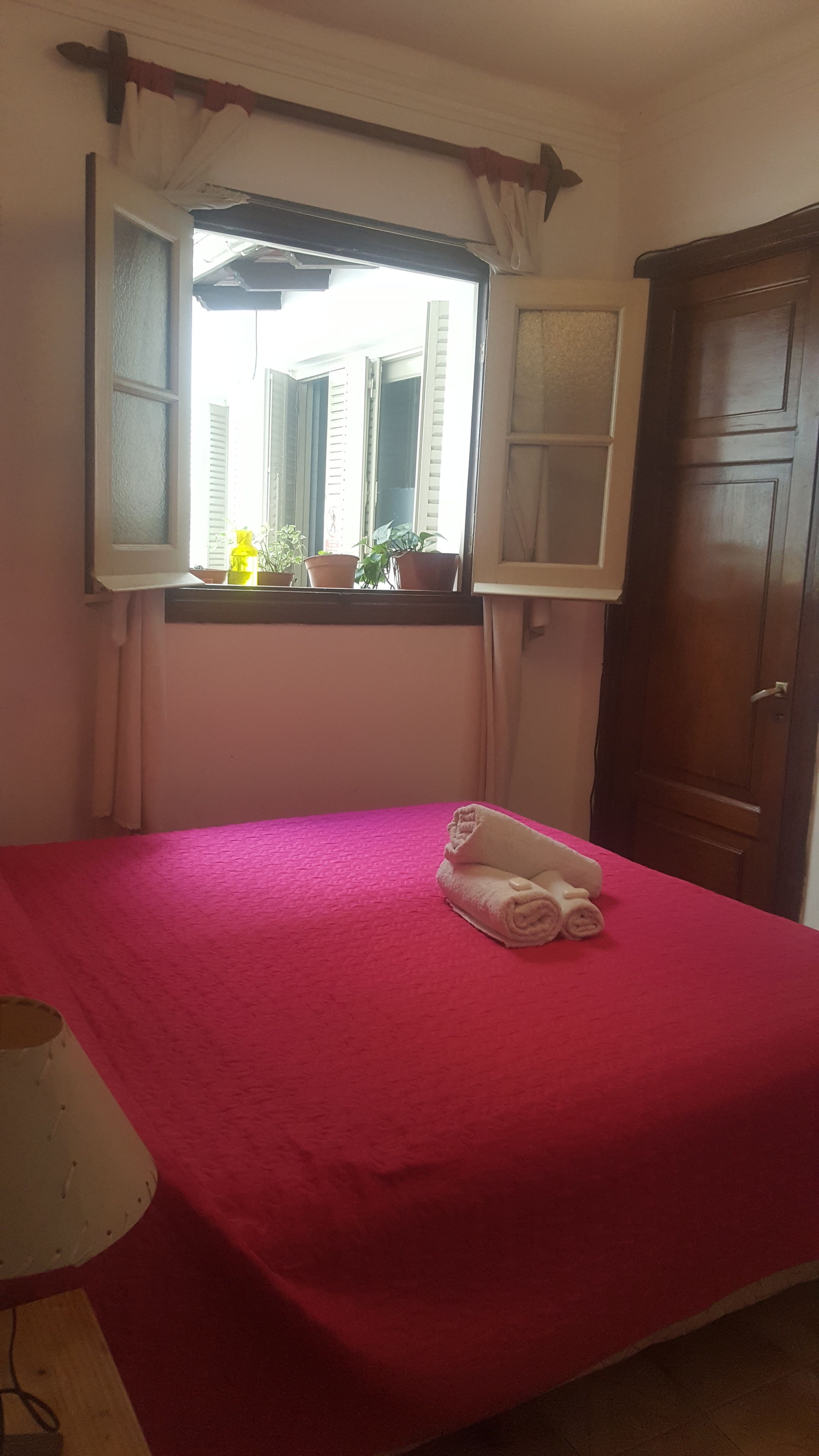 A room with a bed, a window with curtains, a wooden door, and a lamp.