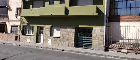 A multi-story building with a green facade, stone lower walls, and a gated entrance.