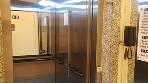 An elevator with a stainless steel interior, a handrail, and a sign listing amenities including rooms, kitchen, bathroom, minibar, TV room, and work packages. - Tapera Hostel (São Paulo)