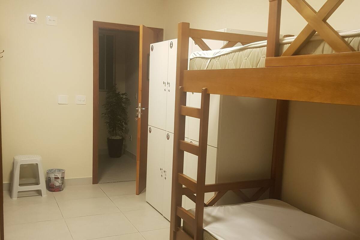 A bunk bed room with a door leading to another room, a small stool, and a trash bin.