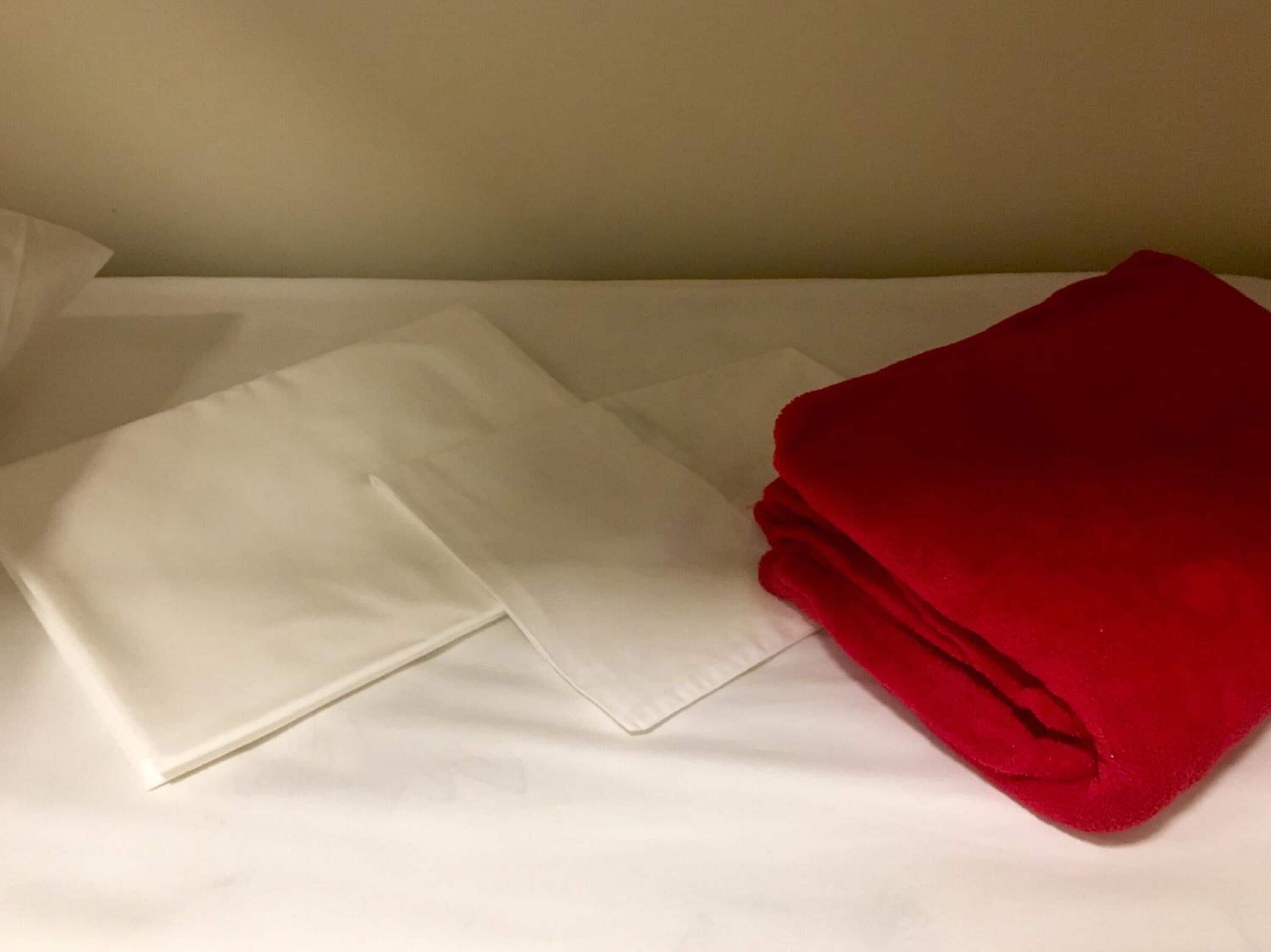 Una cama con sábanas blancas y una manta roja.