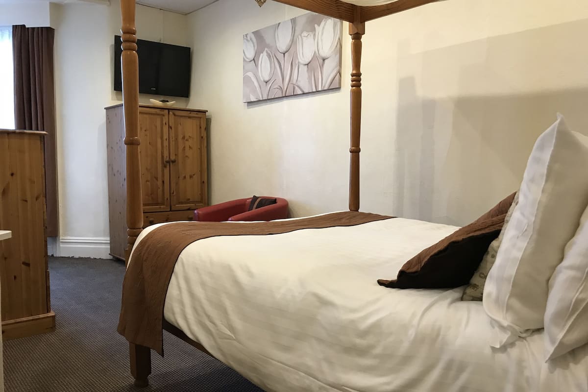 Une chambre à coucher avec un lit à baldaquin, une armoire en bois, un téléviseur à écran plat et un tableau accroché au mur.
