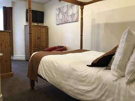 Een slaapkamer met een hemelbed, een houten garderobe, een flatscreen televisie en een schilderij aan de muur.