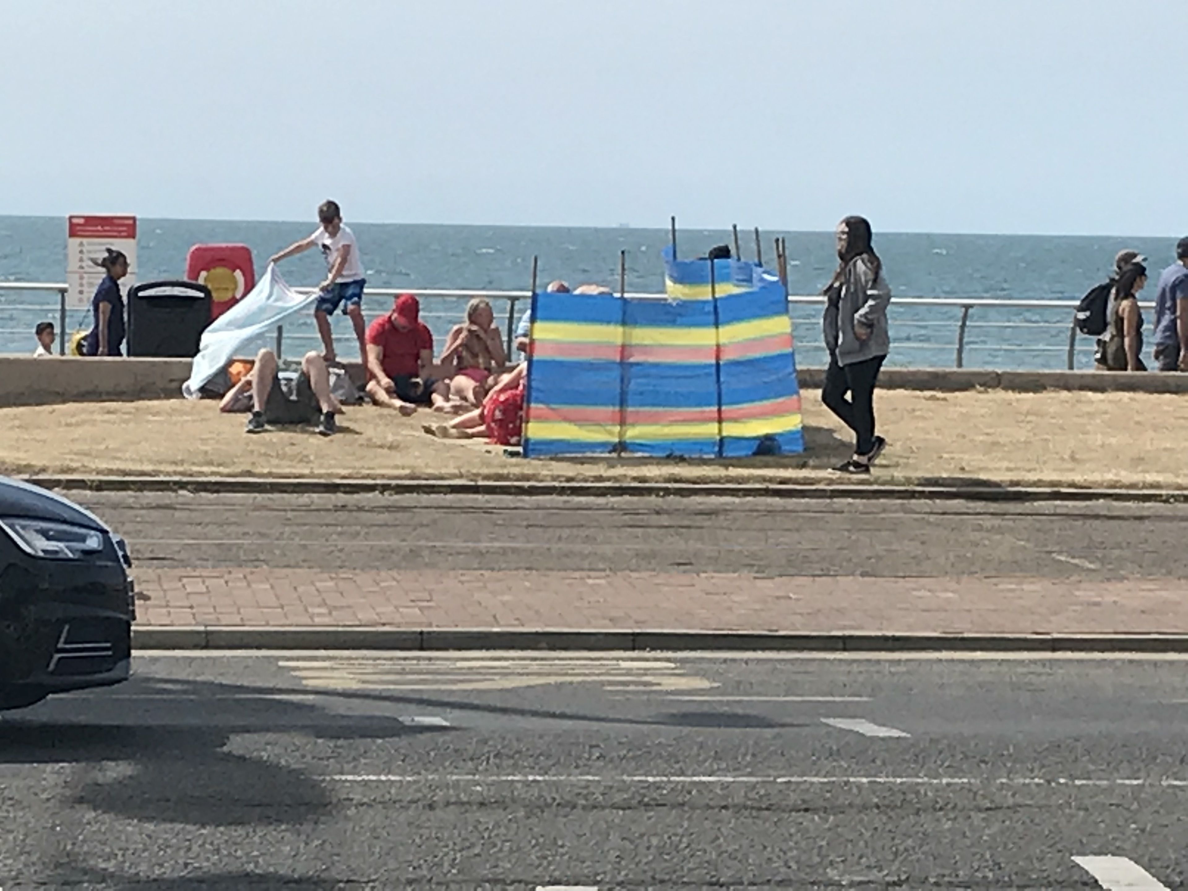 A beachside area with people relaxing and a striped beach umbrella.