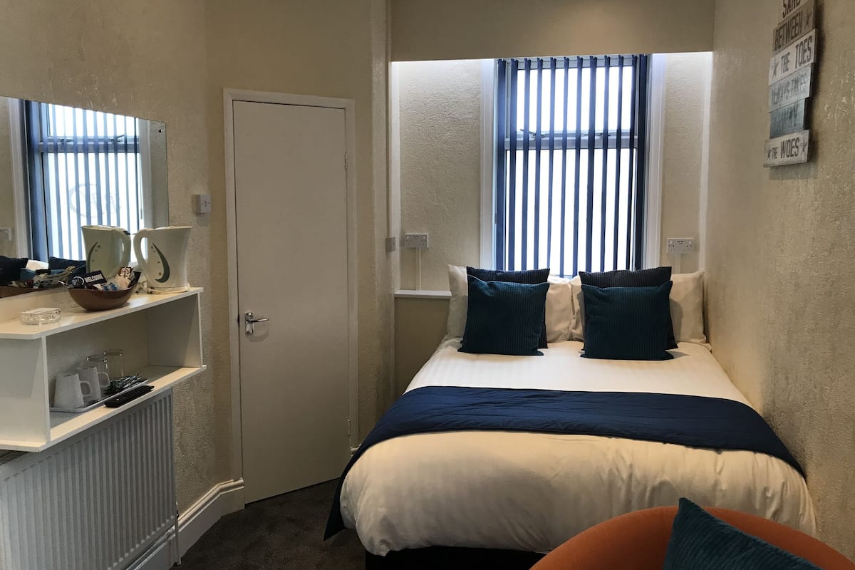 Une chambre d’hôtel avec un lit, un bureau avec un ordinateur, une fenêtre avec des stores et une porte.