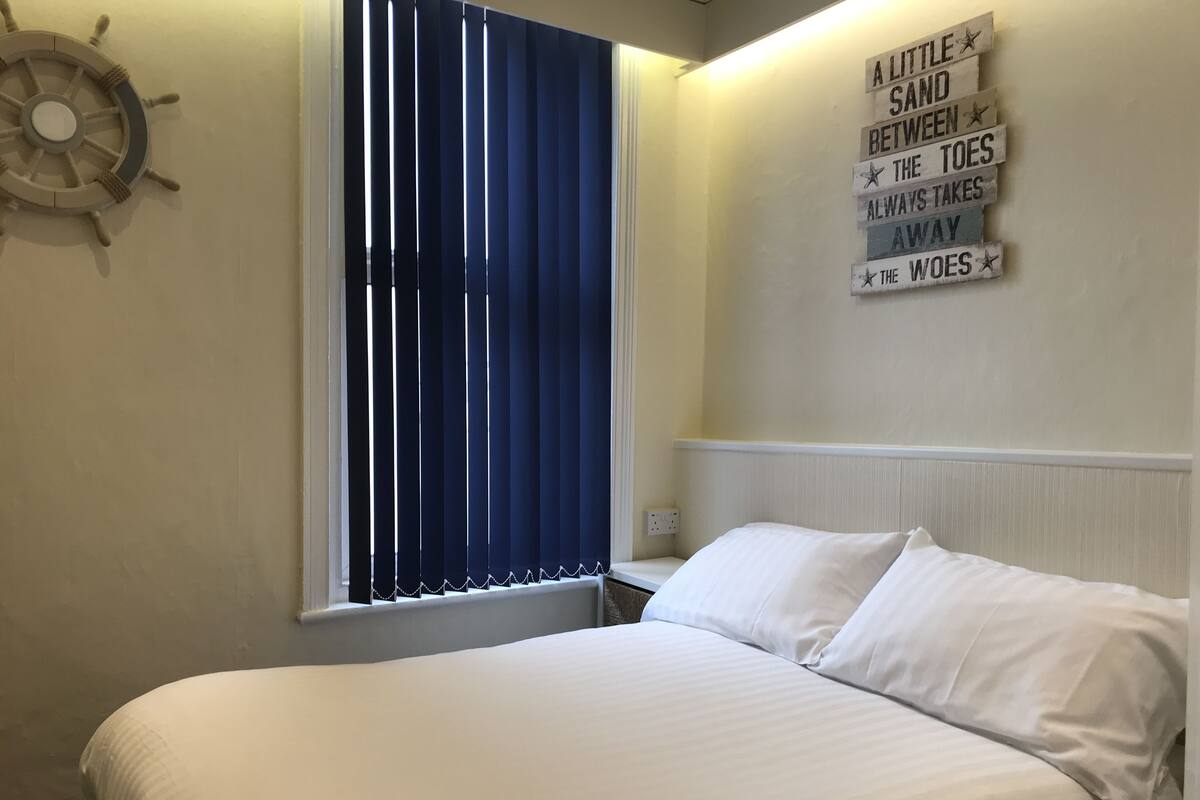 Une chambre à coucher avec un lit, une fenêtre équipée de stores verticaux, un gouvernail de bateau fixé au mur et un panneau affichant une citation inspirante.