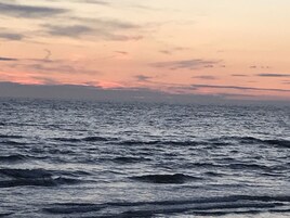 Vista del océano con olas y un atardecer de fondo.
