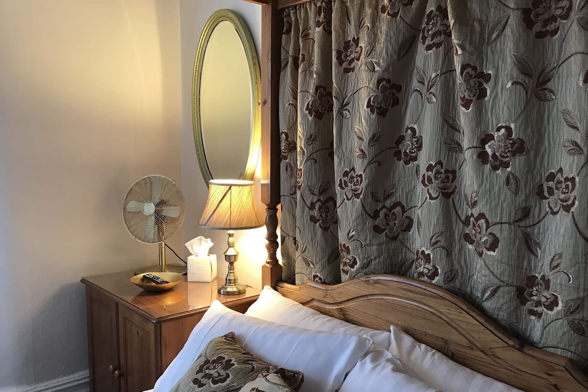 Une chambre à coucher avec un lit, une table de chevet avec une lampe, un miroir et des rideaux à motifs floraux.