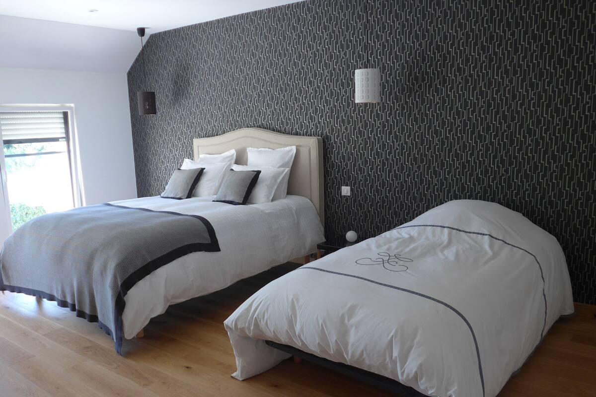 A bedroom with two beds, a patterned wall, and a wooden floor.