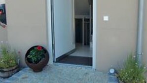 Une porte d’entrée donnant sur un bâtiment dont le hall est carrelé et de part et d’autre duquel on trouve des plantes en pot.